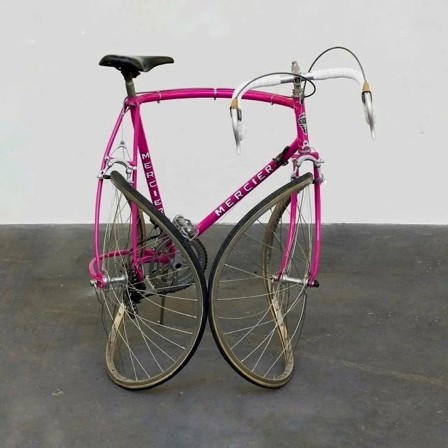 un vélo de course rose plié de façon à ce que le pneu de la roue arrière touche celui de la roue avant