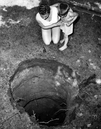 George Brich Mrs. Robert McConnell and son Robert Jr. peer into strange 14 foot cave-in in backyard of their home centre de la terre.jpg