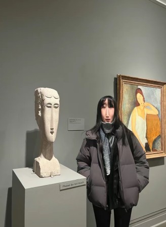 une femme au long nez pose devant une sculpture et un tableau de Modigliani qui lui ressemblent