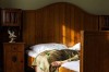 dans la chambre ensoleillée, déjà habillée, une femme agenouillée sur le sol repose encore un peu le haut de son corps en appuyant sa tête sur le lit