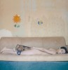 une femme nue allongée à plat ventre sur une banquette beige, un chien déprimé la tête posée sur ses creux polités