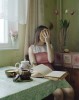 à la table du petit-déjeuner sur laquelle un livre est ouvert, une crêpe en marque-page, une femme s'applique une poignée de pancakes sur le visage