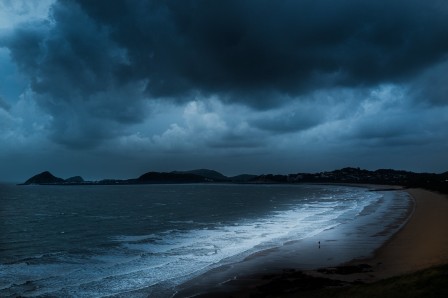 un homme minuscule marchant sur une plage déserte entre la mer et le ciel du même bleu sombre