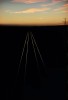 quatre rails sur le sol encore sombre traçant une ligne de fuite lumineuse vers l'infini sous le soleil levant