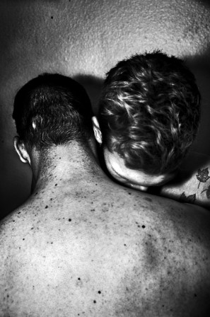 deux hommes torse nu s'étreignent, la tête de chacun appuyée sur l'épaule de l'autre