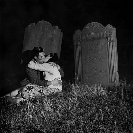 dans un cimetière, assis sur une tombe, deux amoureux s'embrassent