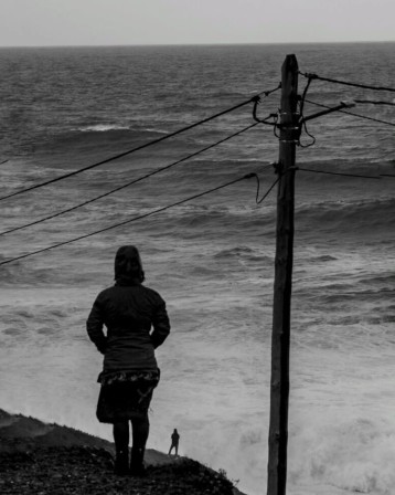 au bord de la mer en hiver, une femme en surplomb regarde un homme au bord de la falaise