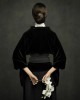 une femme en noir, de dos, tient derrière elle des fleurs blanches