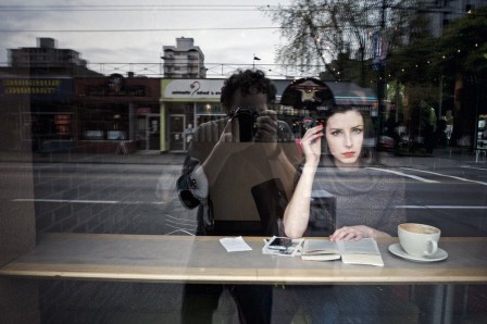 Alice prenant une boisson chaude dans un café photographiée de la rue à travers la vitrine