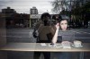 Alice prenant une boisson chaude dans un café photographiée de la rue à travers la vitrine