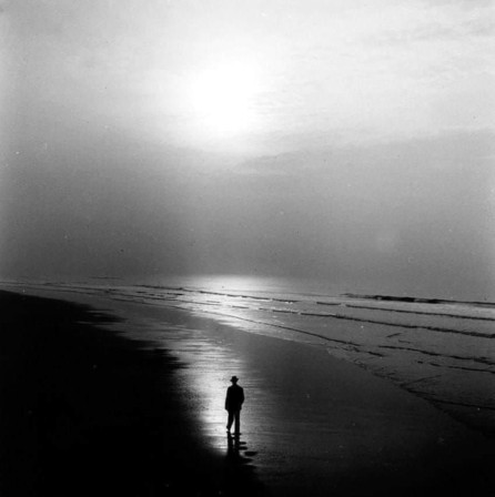 dans une lumière incertaine, un homme en chapeau sur une immense plage sinistrogyre