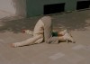 sur le trottoir, une femme à genoux, la tête entre les jambes et les bras tendus, dans la posture d'une roulade avant interrompue