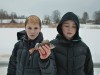 debout dans la neige en doudoune noire, deux jeunes garçons tiennent un petit poisson gelé