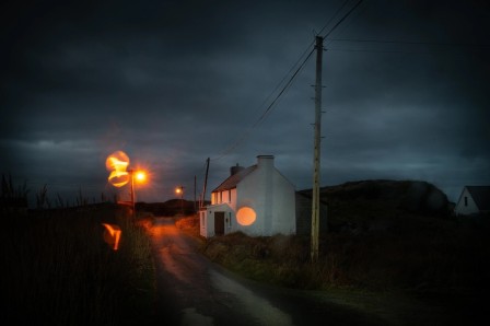 peu avant le lever du jour, au bord de la mer une maison isolée sur un chemin, les lampadaires comme des boules de feu