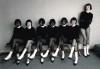 six femmes noires et blanches sur un banc, la septième debout