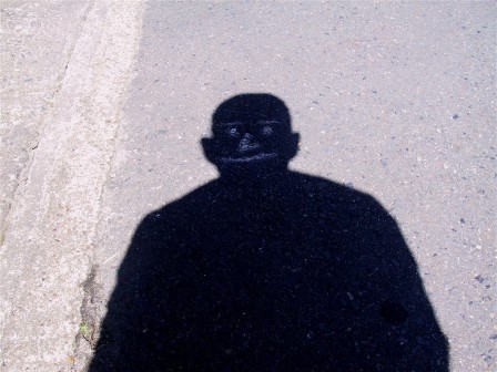 l'ombre d'un homme sur le trottoir, la tête calée sur le dessin à la craie d'un visage